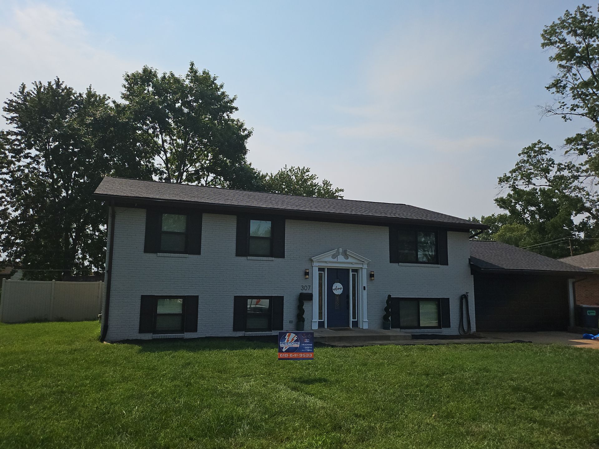 Completed dark architectural shingle roof on a white-painted brick split-level home with black shutters in Mascoutah, IL