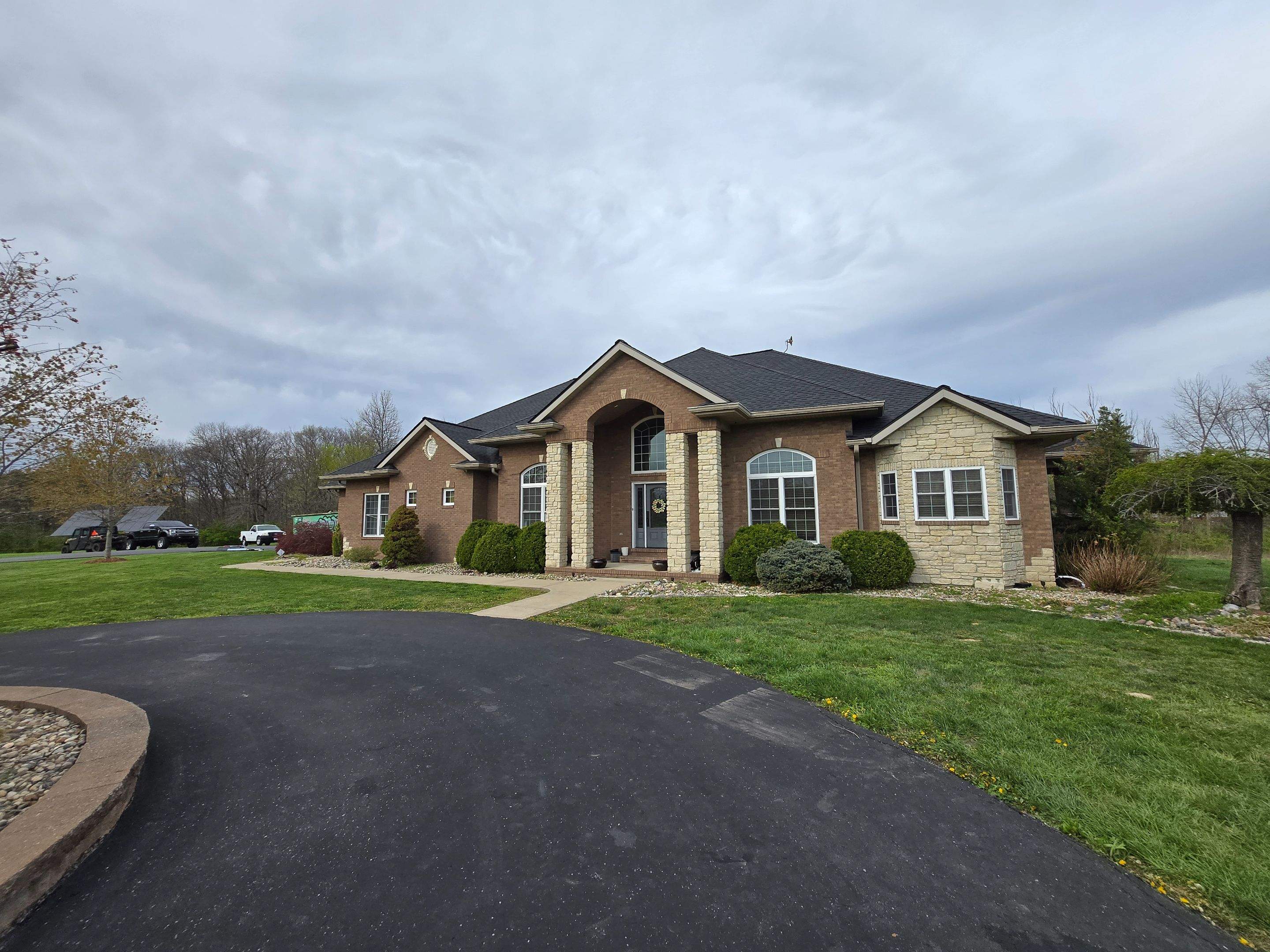 Completed dark architectural shingle roof on a large brick and stone ranch home with an arched portico entry in Millstadt, IL