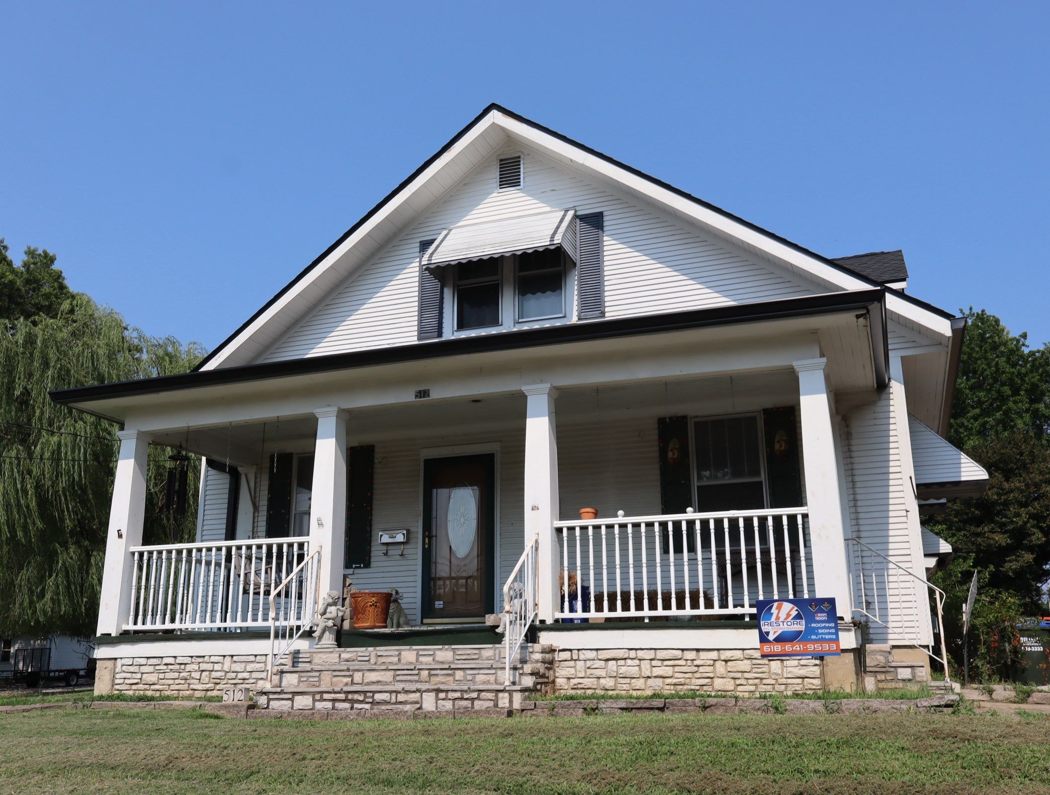 Completed dark architectural shingle roof on a white two-story home with a full-width covered front porch in Waterloo, IL