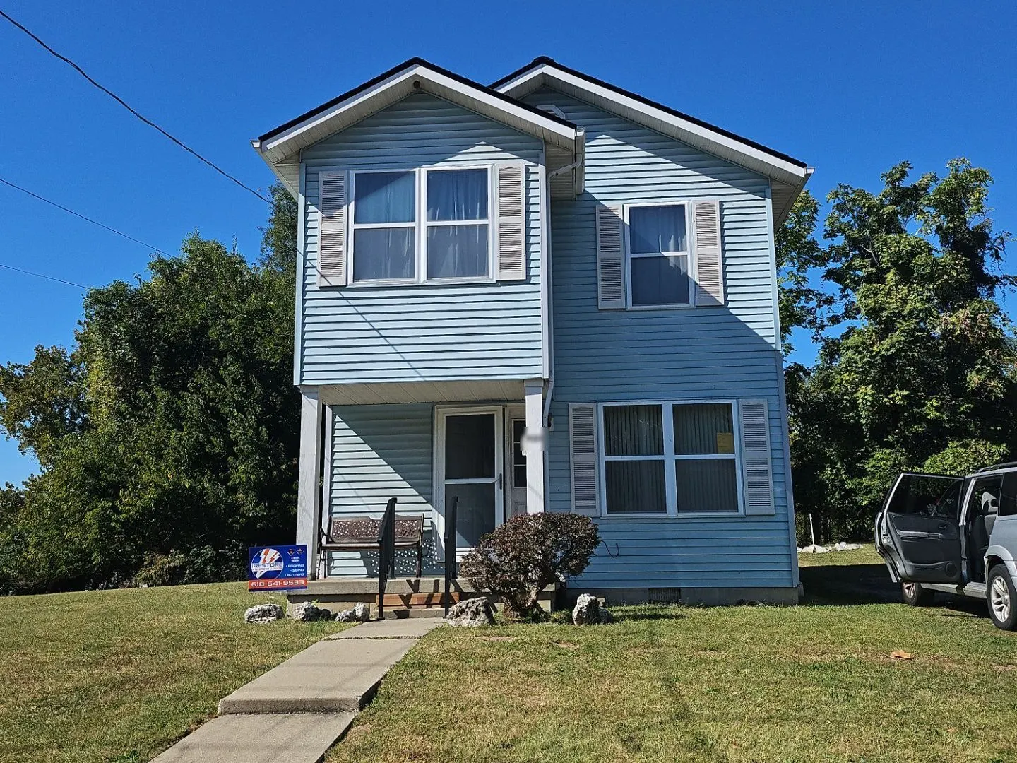 Finished roof, light blue vinyl siding and gutters on a two-story home in Alton, IL, with an iRestore STL yard sign out front