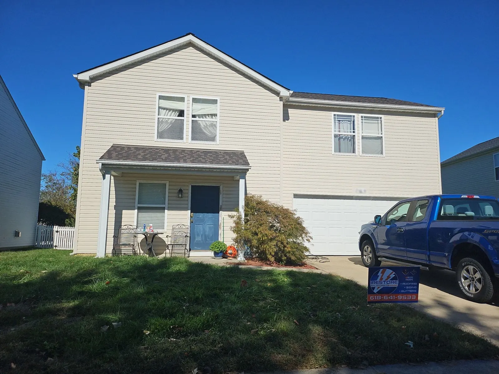 New brown architectural shingle roof on a cream-sided two-story home in Mascoutah, IL, with an iRestore STL yard sign out front