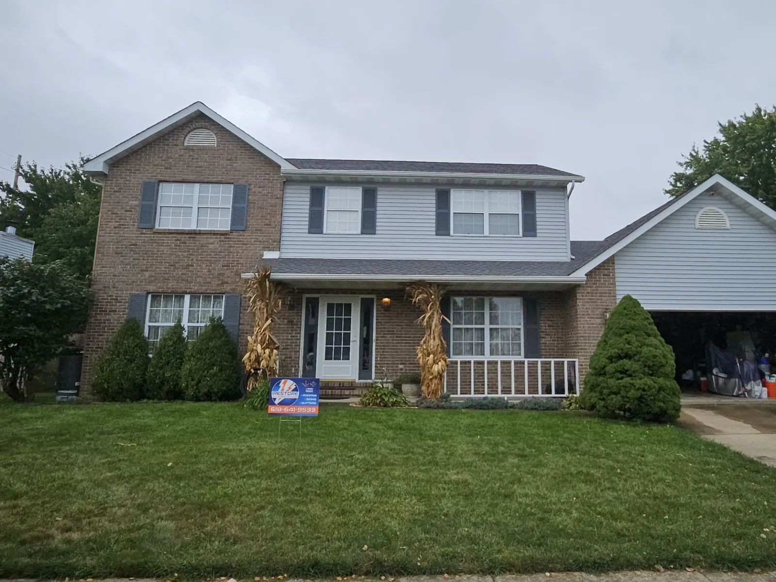 New architectural shingle roof on a brick and gray-sided two-story home in O'Fallon, IL, with an iRestore STL yard sign in the front lawn